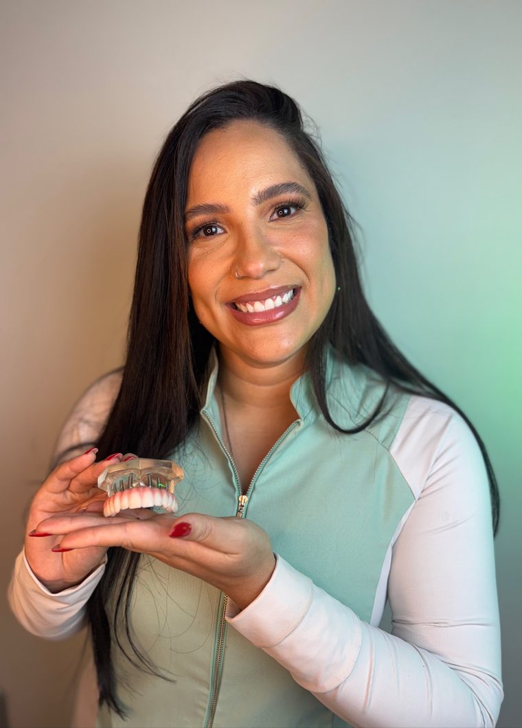 Dra. Tayane Pierrout segurando um modelo de prótese protocolo sobre implantes, na Vem Sorrir em Anchieta